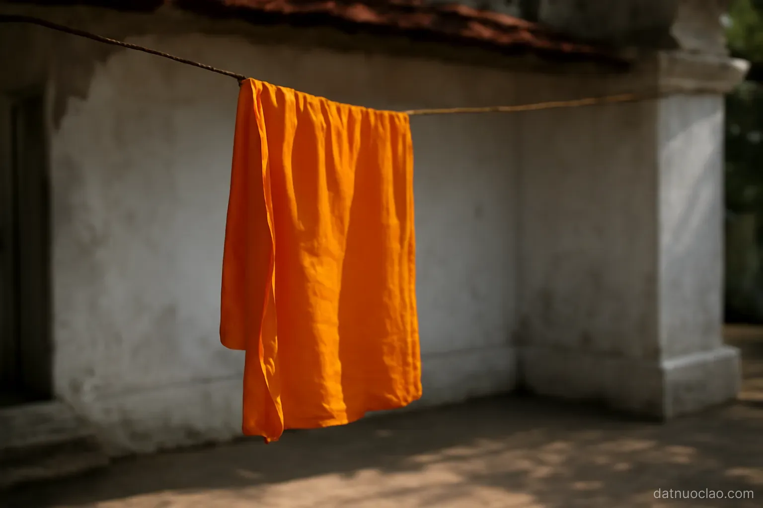 Saffron cloth hanging on a line inside a temple compound, whitewashed wall and shade, morning